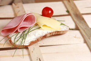 A piece of bread with ham, cheese, tomato, and spread